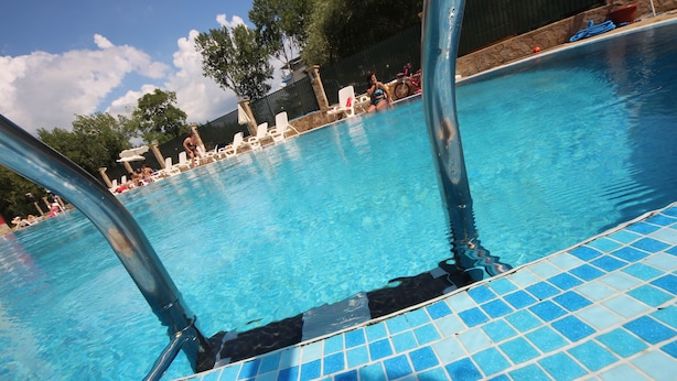 A swimming pool with clear blue water, surrounded by lounge chairs and a stone wall. - Menada Global Ville Apartments (Sunny Beach)