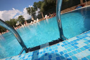 Une piscine à l’eau d’un bleu cristallin, entourée de chaises longues et d’un mur en pierre.