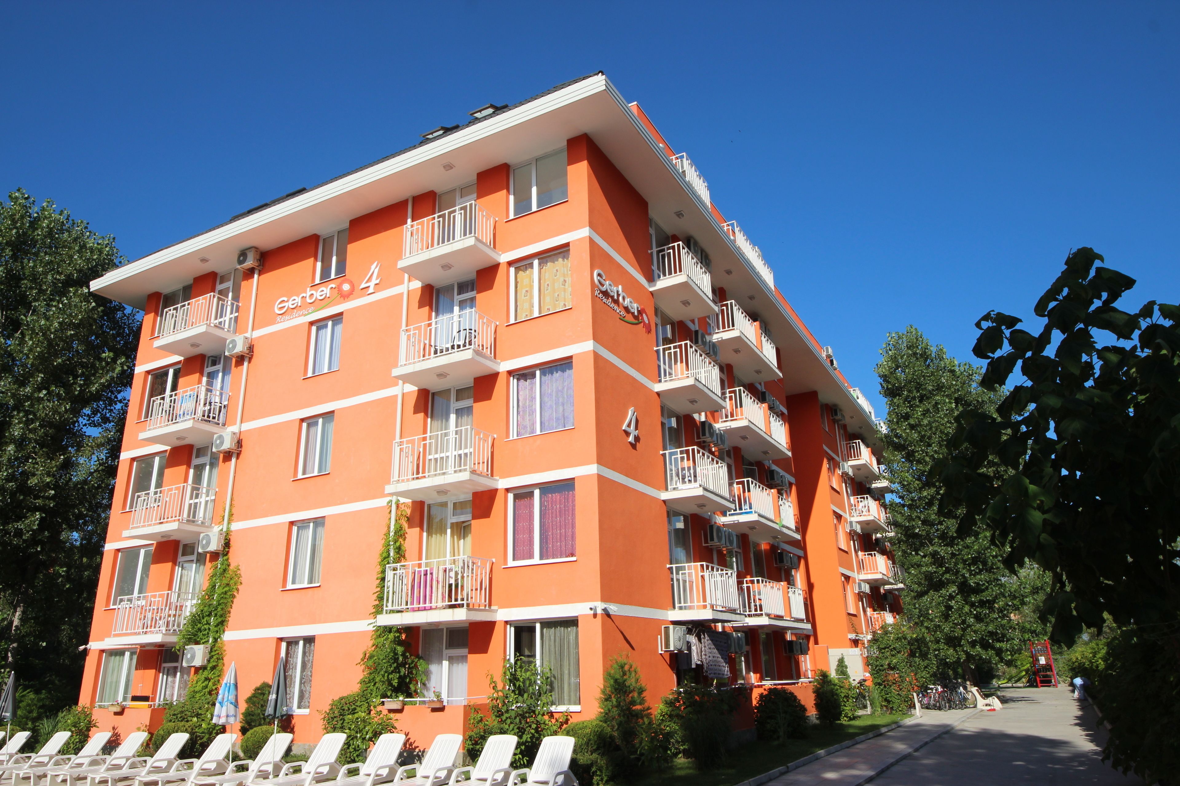 A multi-story hotel with balconies, a clear sky, and a well-maintained garden area.