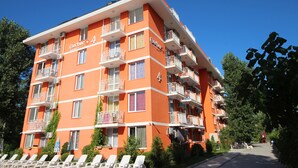 Un hotel a più piani con balconi, un cielo sereno e un giardino curato.