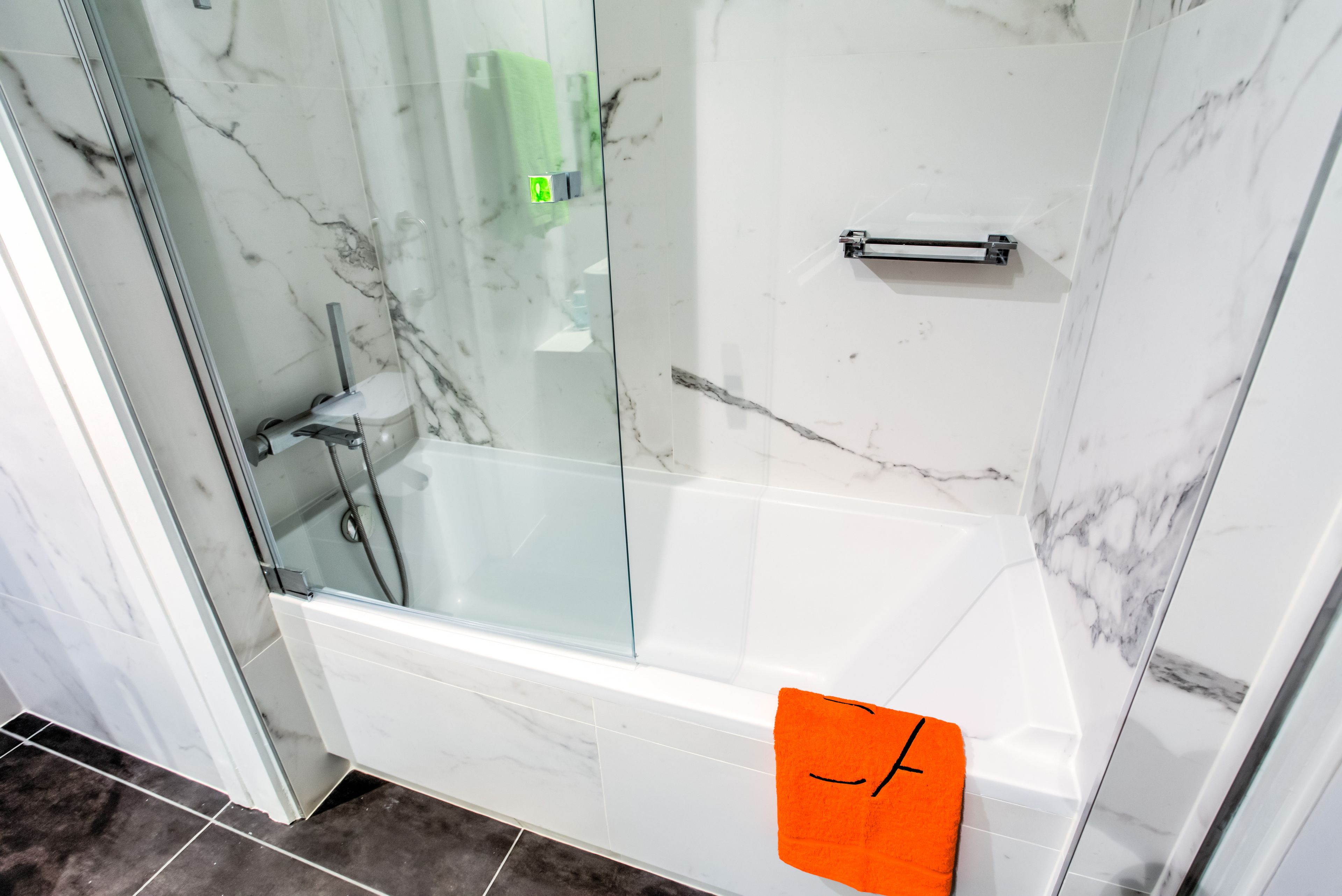 Une salle de bain dotée d’une douche à parois de verre, d’une baignoire blanche et d’un mur recouvert de carreaux de marbre.