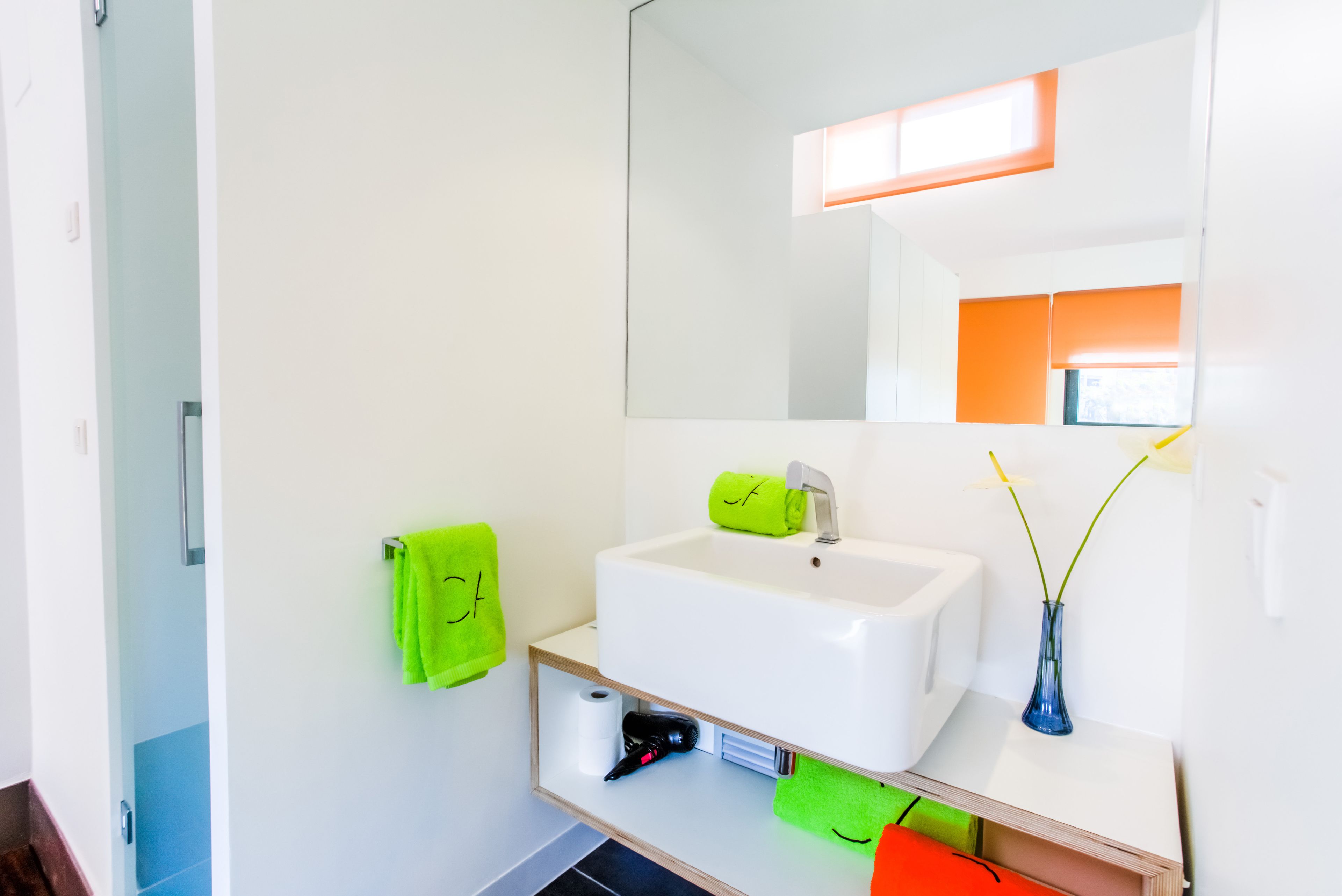 Une salle de bain moderne avec un lavabo blanc, un miroir et un porte-serviettes sur lequel est posée une serviette verte.
