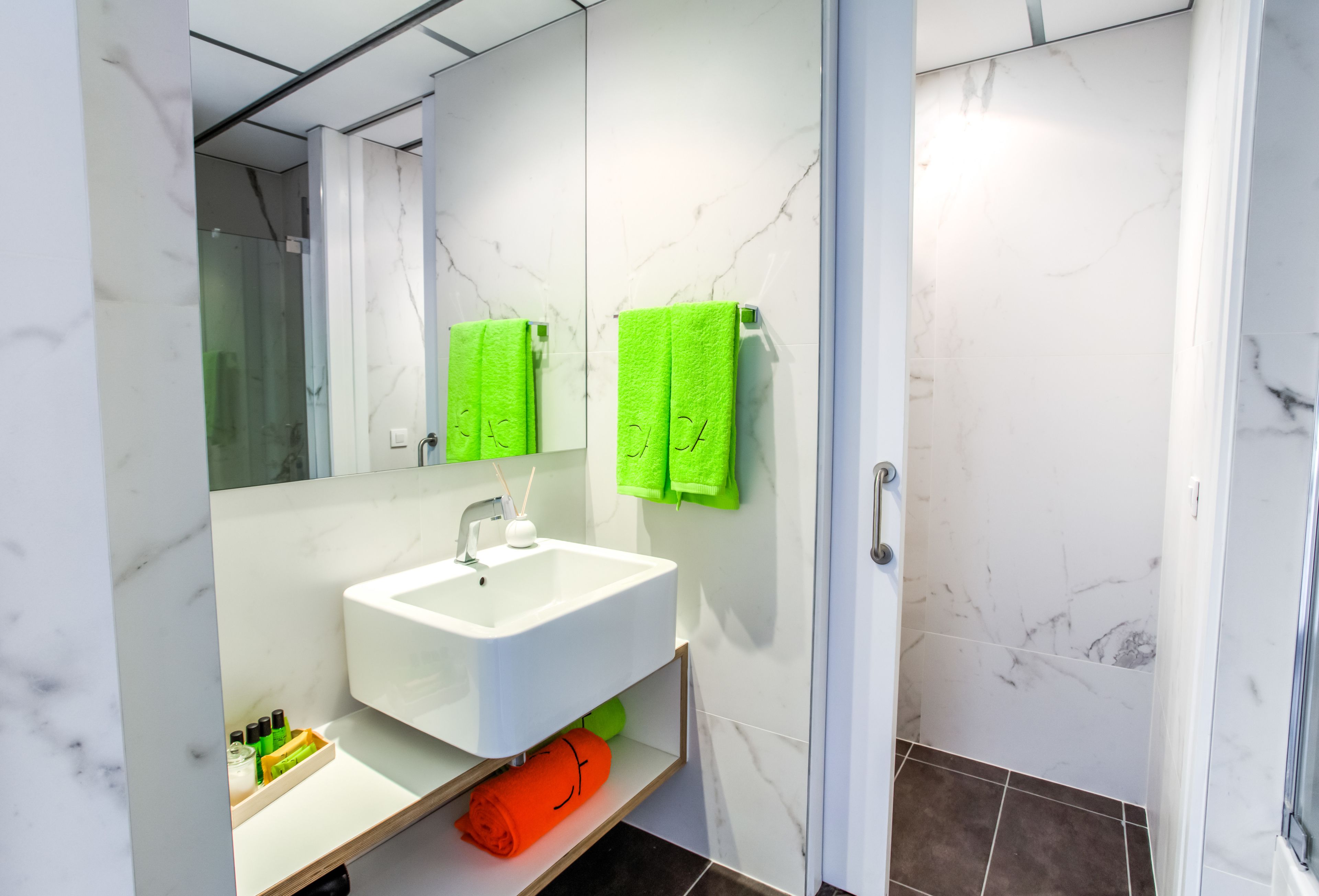 Ein modernes Badezimmer mit einem weißen Waschbecken, grünen Handtüchern und einer Duschkabine aus Glas.