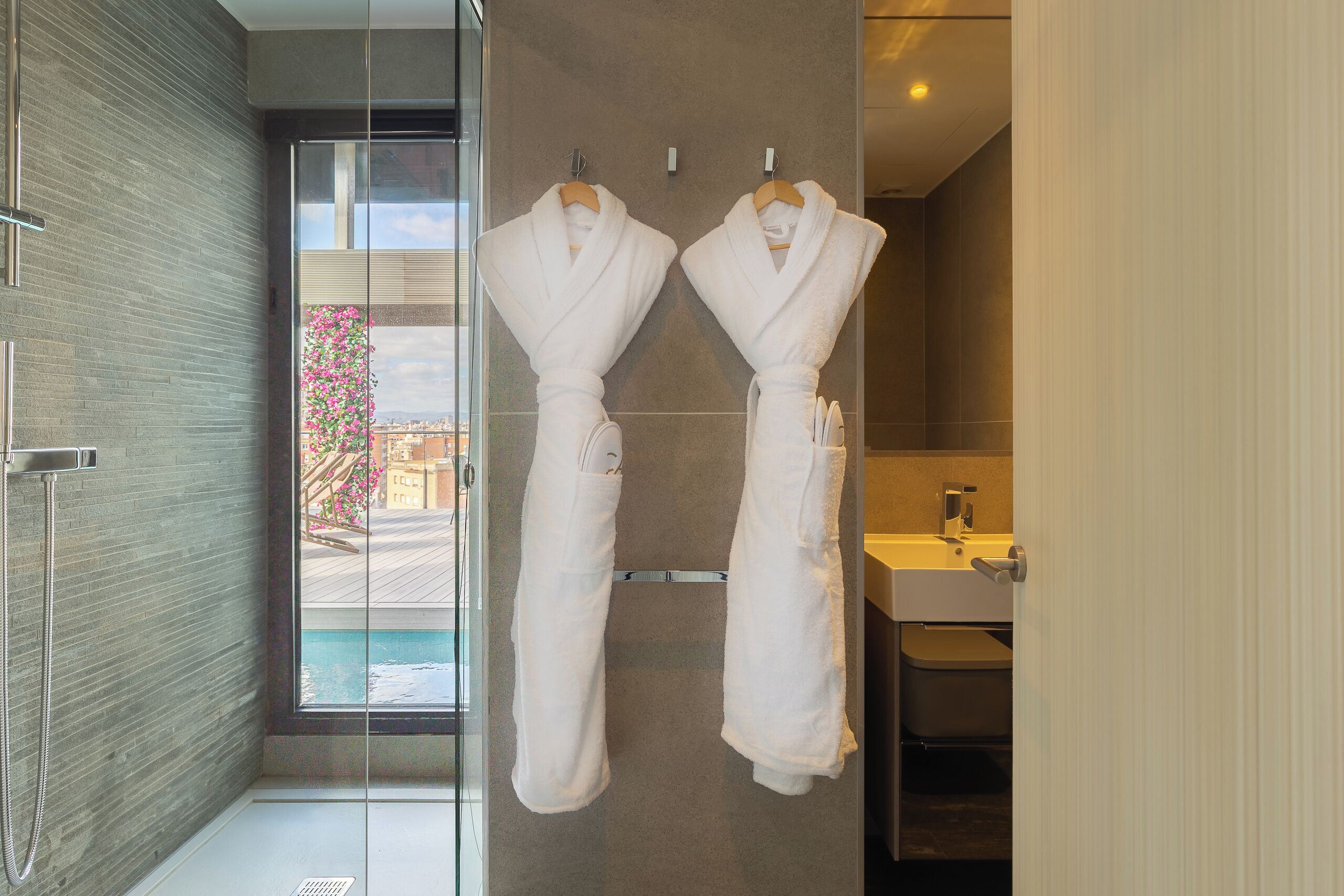 A modern bathroom with a glass shower enclosure, a built-in sink, and two white robes hanging on a rack.