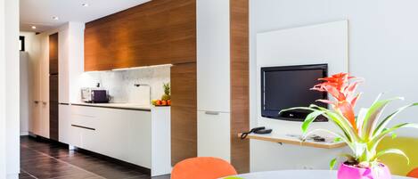A modern kitchen with white cabinets, a wooden accent wall, a built-in oven, and a small island with a microwave.