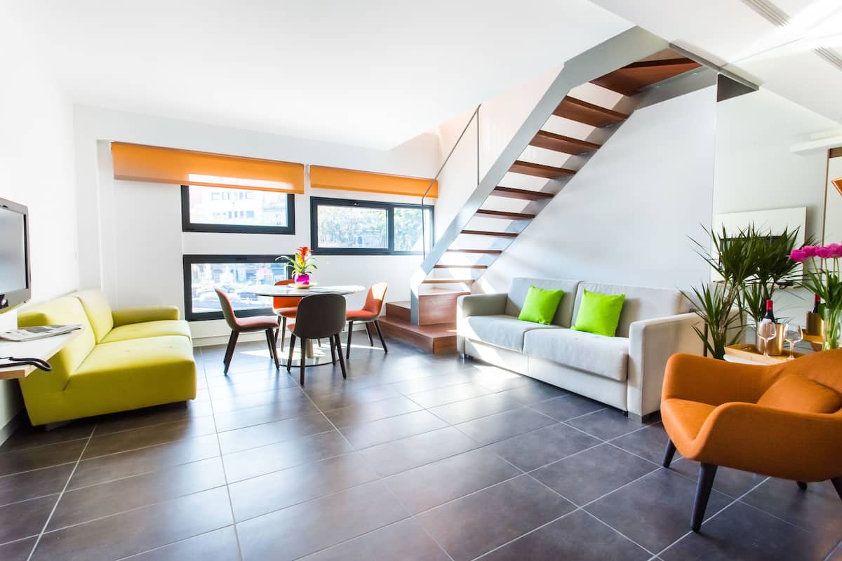A modern living room with a staircase, a dining area, and a sofa with green cushions.
