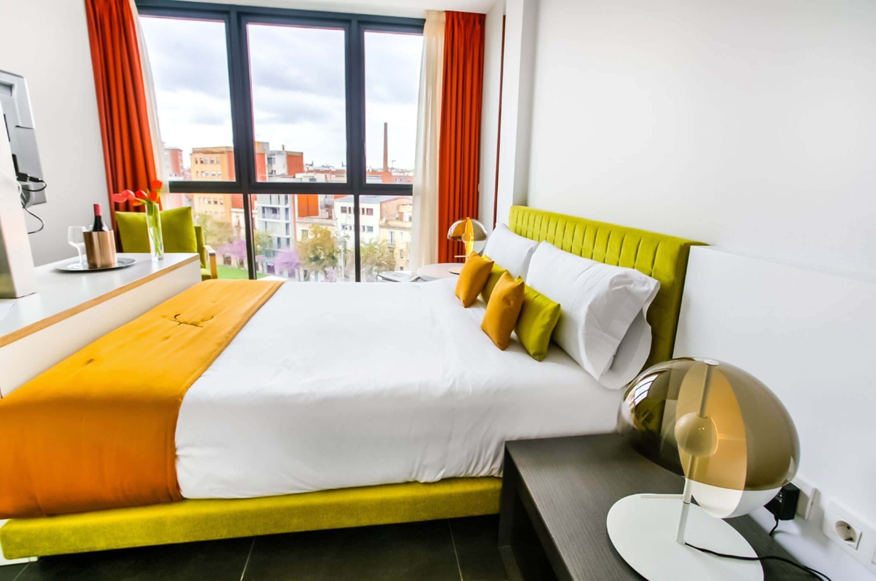 Una habitación de hotel moderna con una cama grande, un escritorio y vistas a la ciudad a través de amplios ventanales.