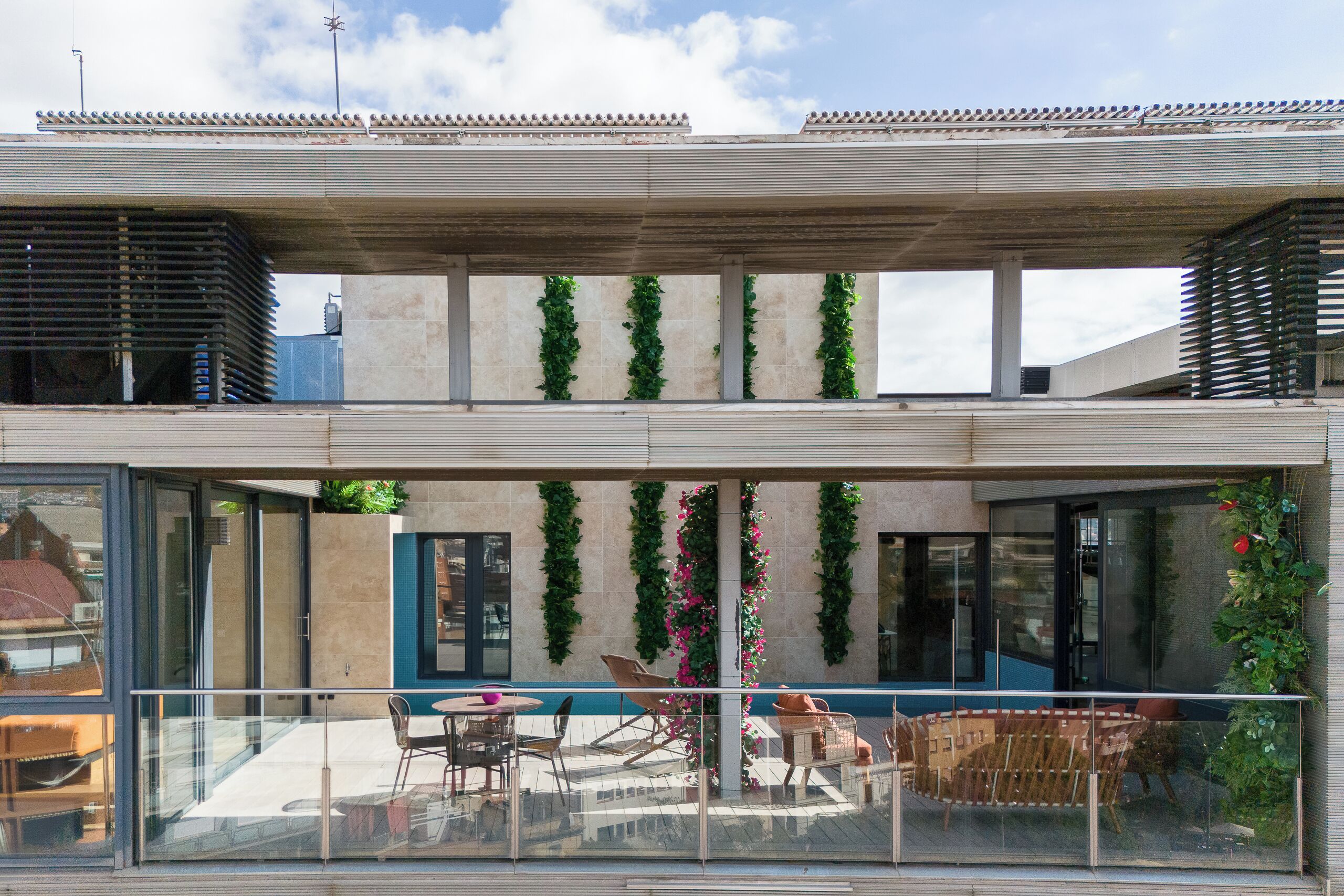 Un edificio moderno con fachada de vidrio, zona de estar al aire libre y follaje decorativo.