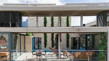 Un edificio moderno con fachada de vidrio, zona de estar al aire libre y follaje decorativo.