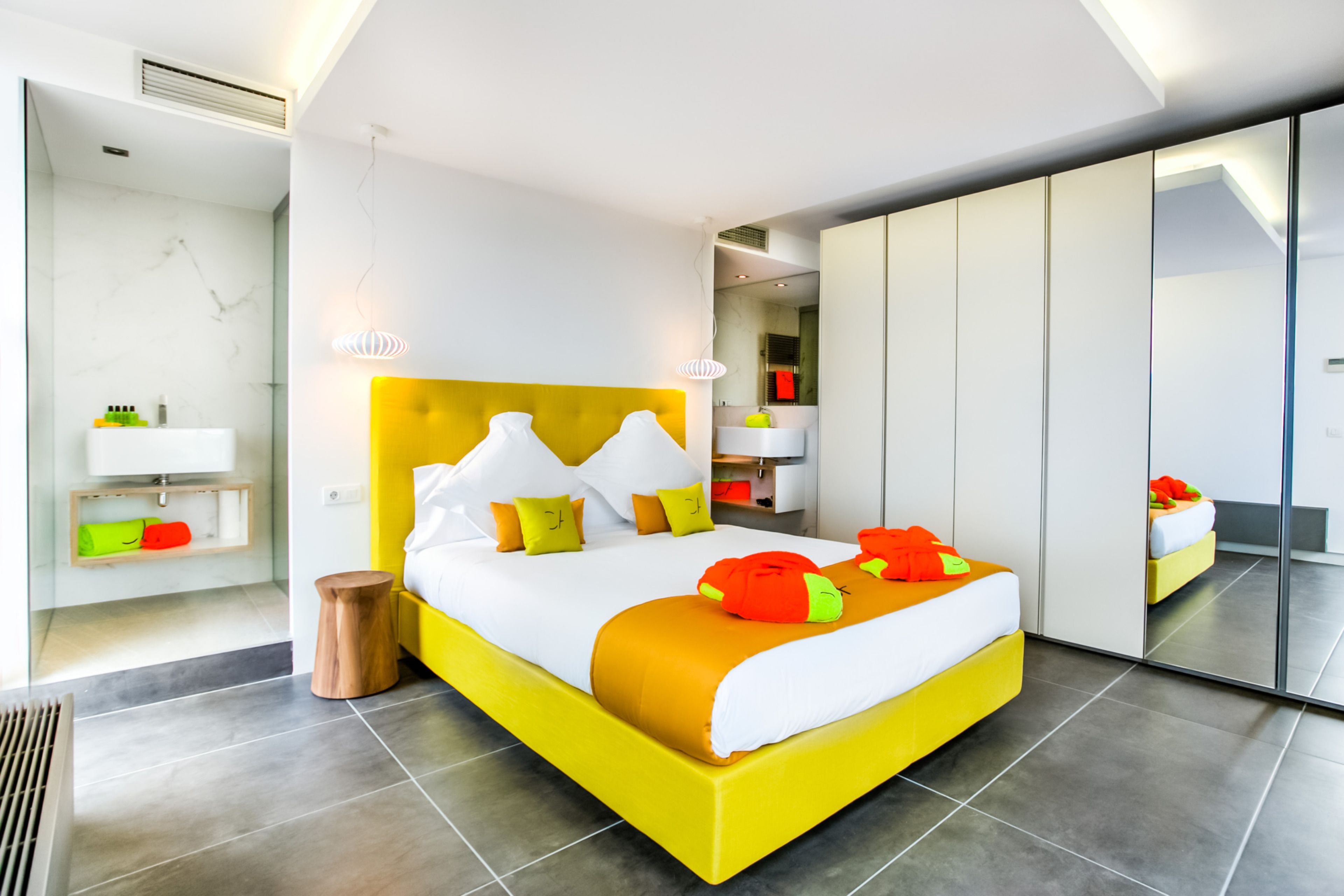 A modern bedroom with a bright yellow bed, white bedding, and a large mirror.