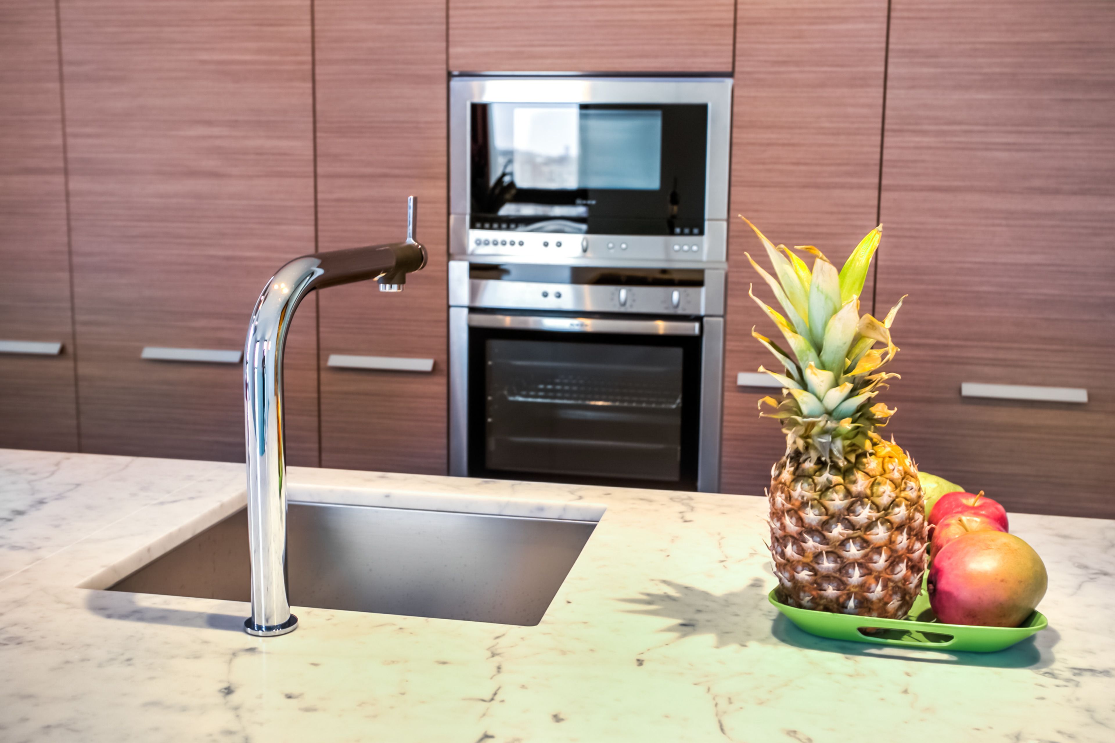Una cocina con un lavamanos de acero inoxidable, un horno empotrado y un microondas encima.