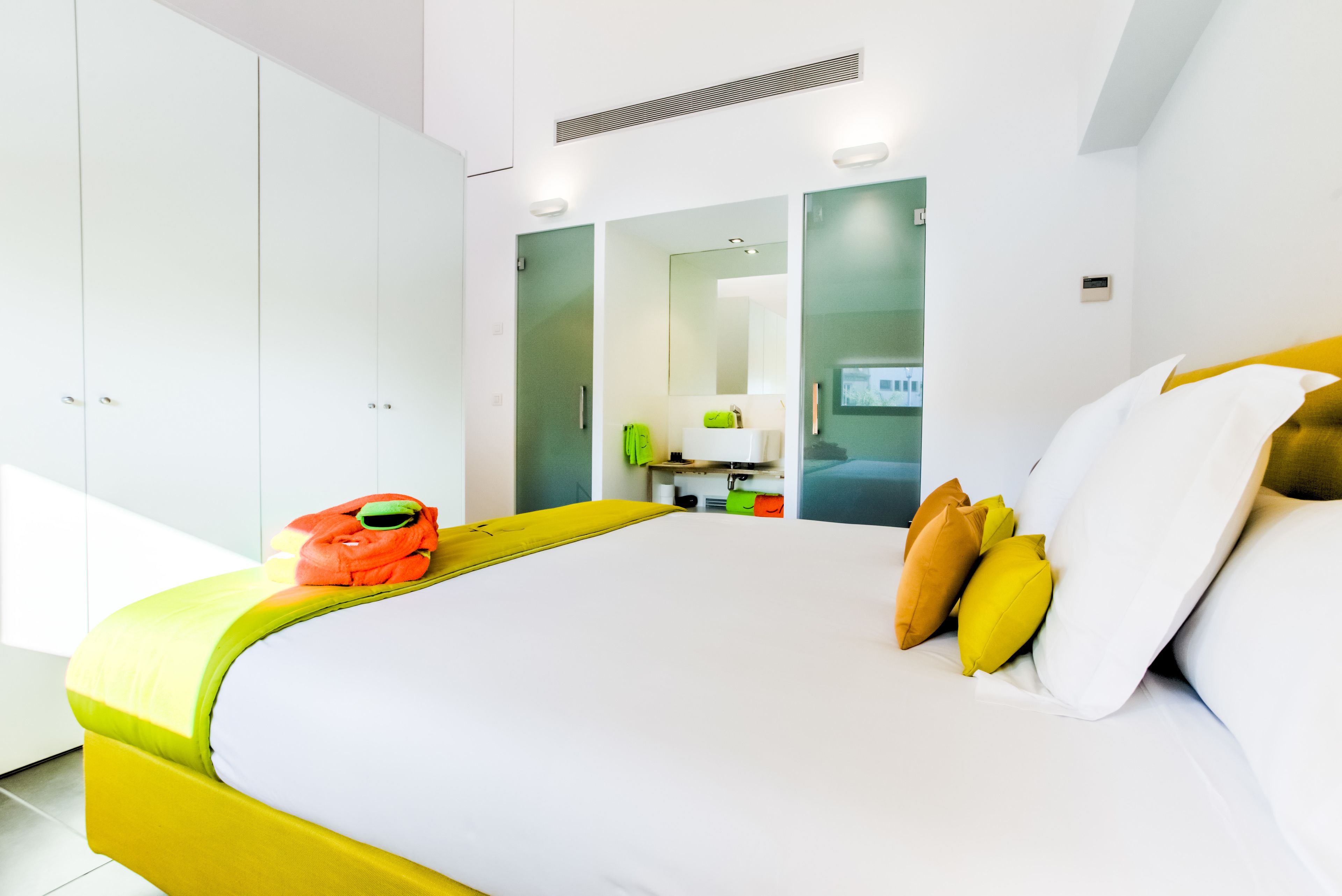 Una habitación de hotel moderna con una cama grande, un armario, un baño con espejo y un escritorio pequeño.