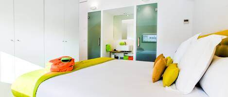 Una habitación de hotel moderna con una cama grande, un armario, un baño con espejo y un escritorio pequeño.