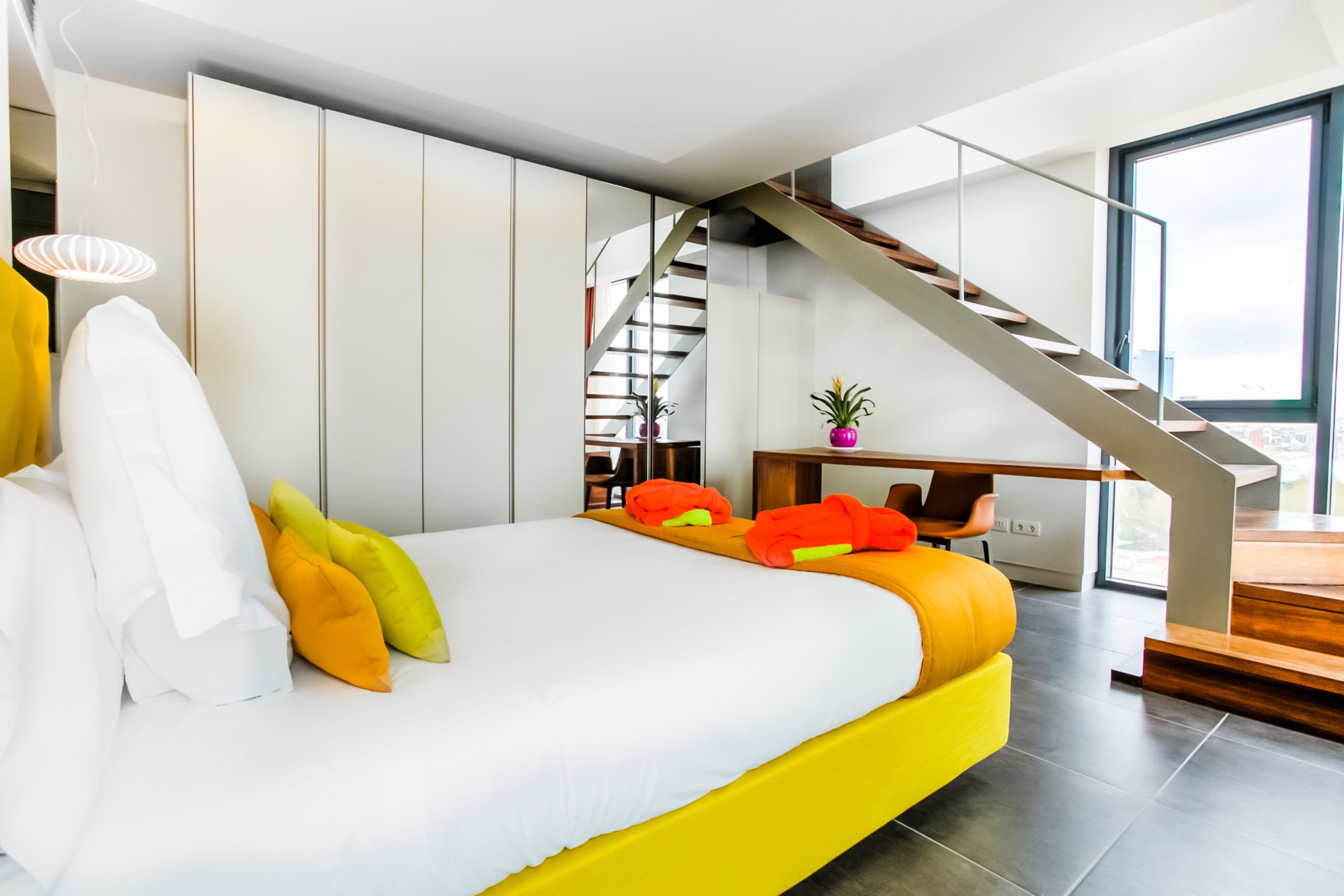 A modern bedroom with a large bed, a staircase, and a desk area.