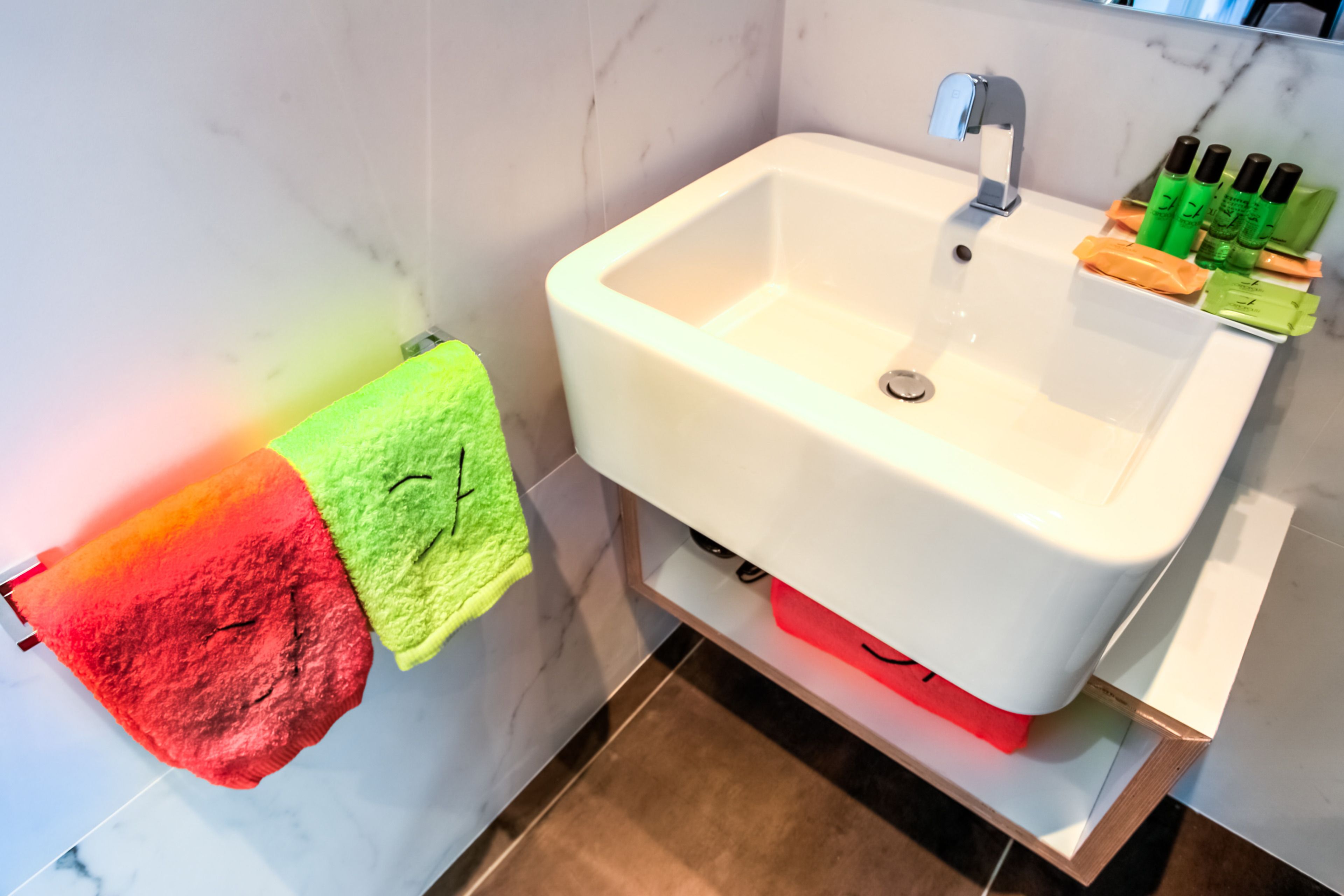 A bathroom with a white sink, a mirror, and a shelf with toiletries.