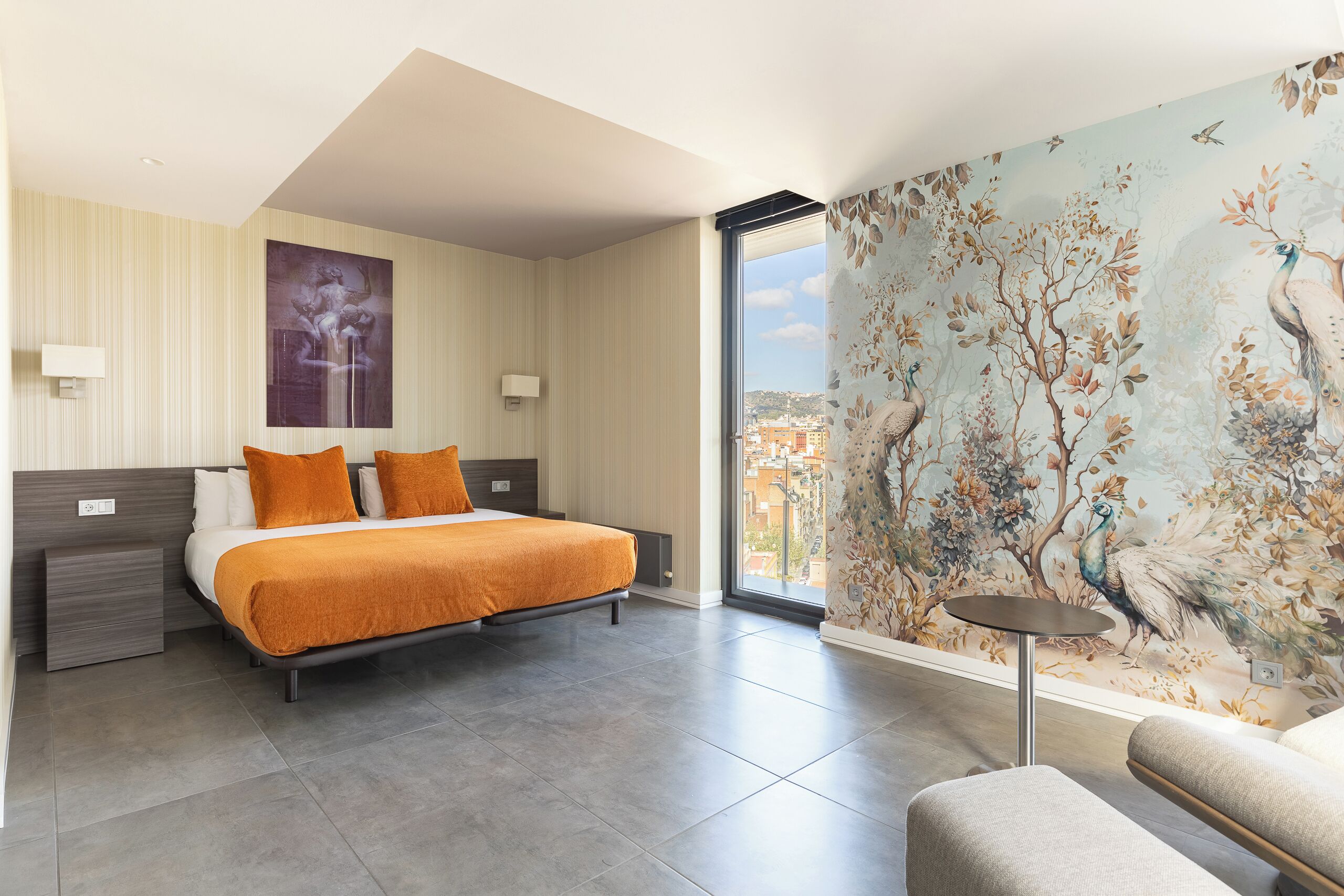 A modern hotel room with a large bed, a view of the city, and a mural of birds and trees.