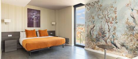 A modern hotel room with a large bed, a view of the city, and a mural of birds and trees.
