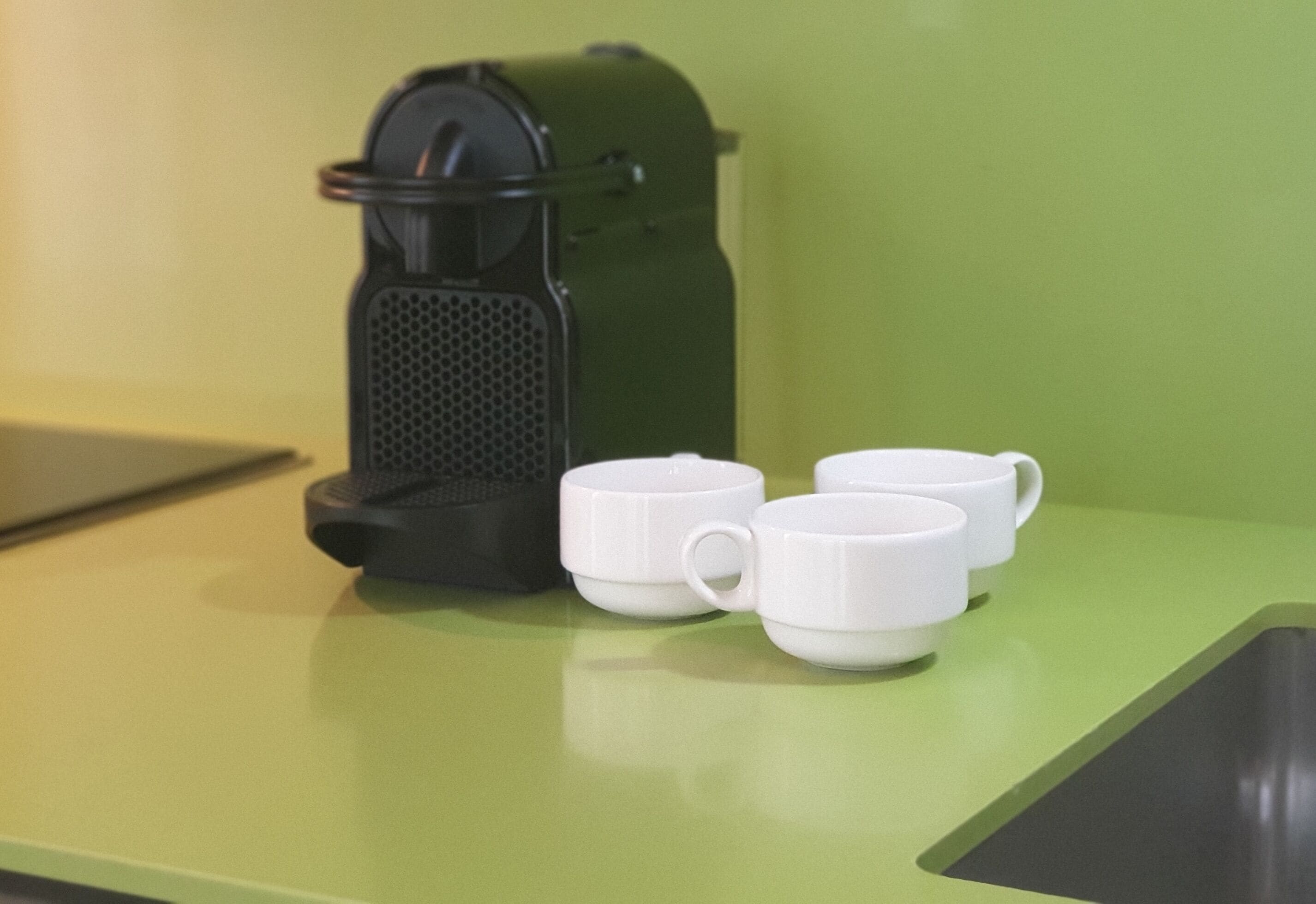 A coffee maker and three white cups on a green countertop.