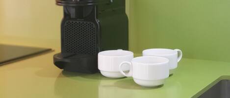 A coffee maker and three white cups on a green countertop.