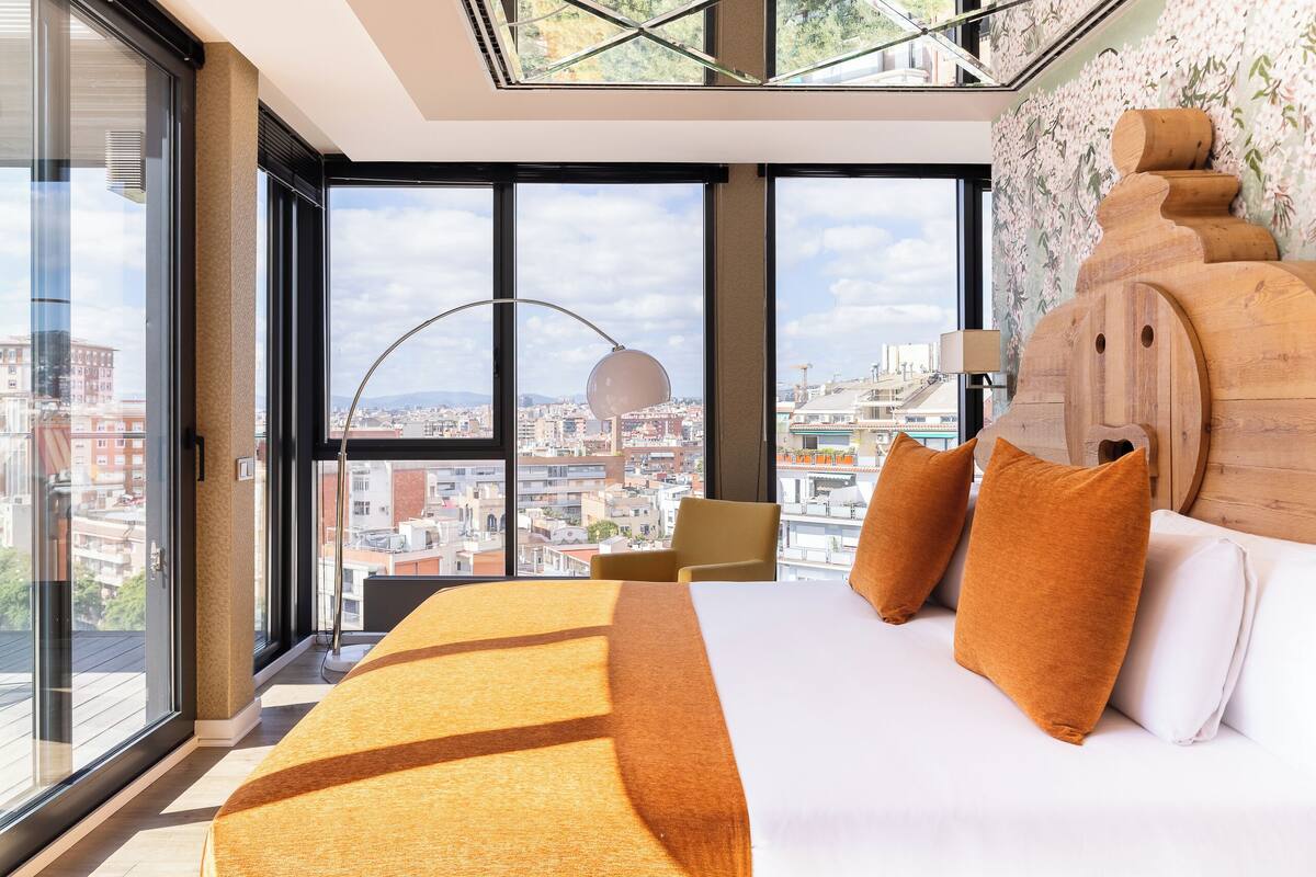 A modern hotel room with a large bed, a view of the city, and a skylight.