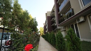 A pathway flanked by greenery and a building with balconies and air conditioning units. - Menada VIP Park Apartments (Sunny Beach)