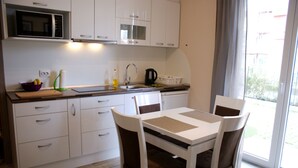 A modern kitchen with white cabinets, a microwave, a sink, and a dining area with a table and chairs. - Menada VIP Park Apartments (Sunny Beach)