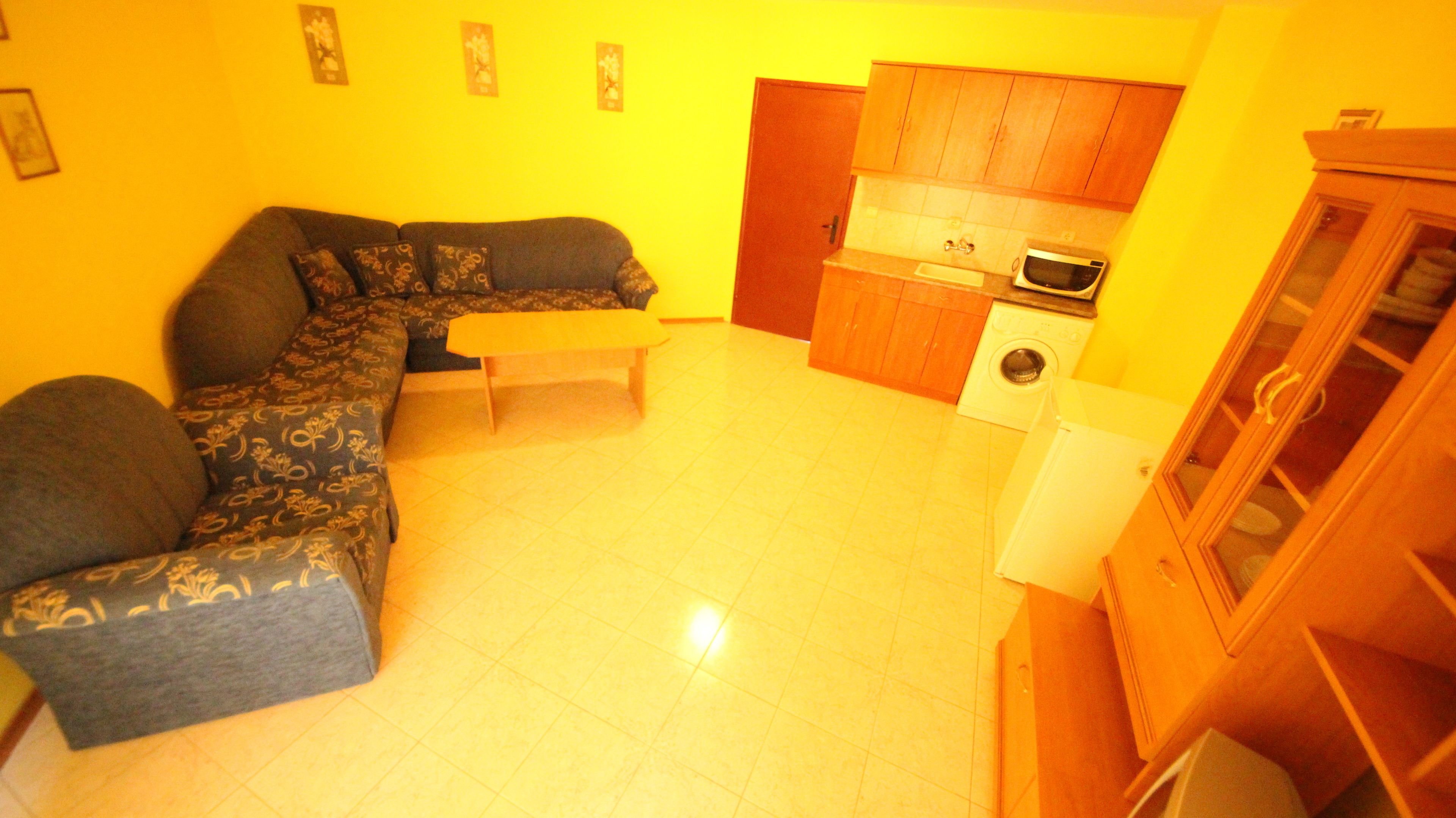 Un salón con sofá, una mesita y una zona de cocina con microondas y lavadora.