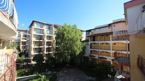 Edificio residencial con varios balcones, un patio central con banca y vegetación circundante.