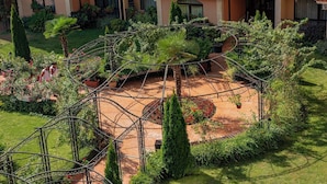 A courtyard with a central circular garden, surrounded by a metal fence, and a building with balconies in the background. - Menada Diamant Residence Apartments (Sunny Beach)
