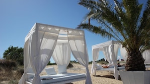 A beachside bed with a canopy, a palm tree, and a sandy beach in the background. - Menada Diamant Residence Apartments (Sunny Beach)