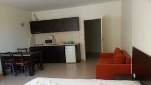 Et hotelværelse med en seng, et spisebord med stole, et tekøkken og en rød sofa.