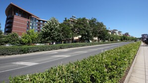 En moderne bygning med en buet facade og flere balkoner, omgivet af velholdt beplantning og en klar, blå himmel.