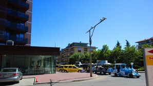 En gade med et blåt tog, gule biler og en bygning med en glasfacade.