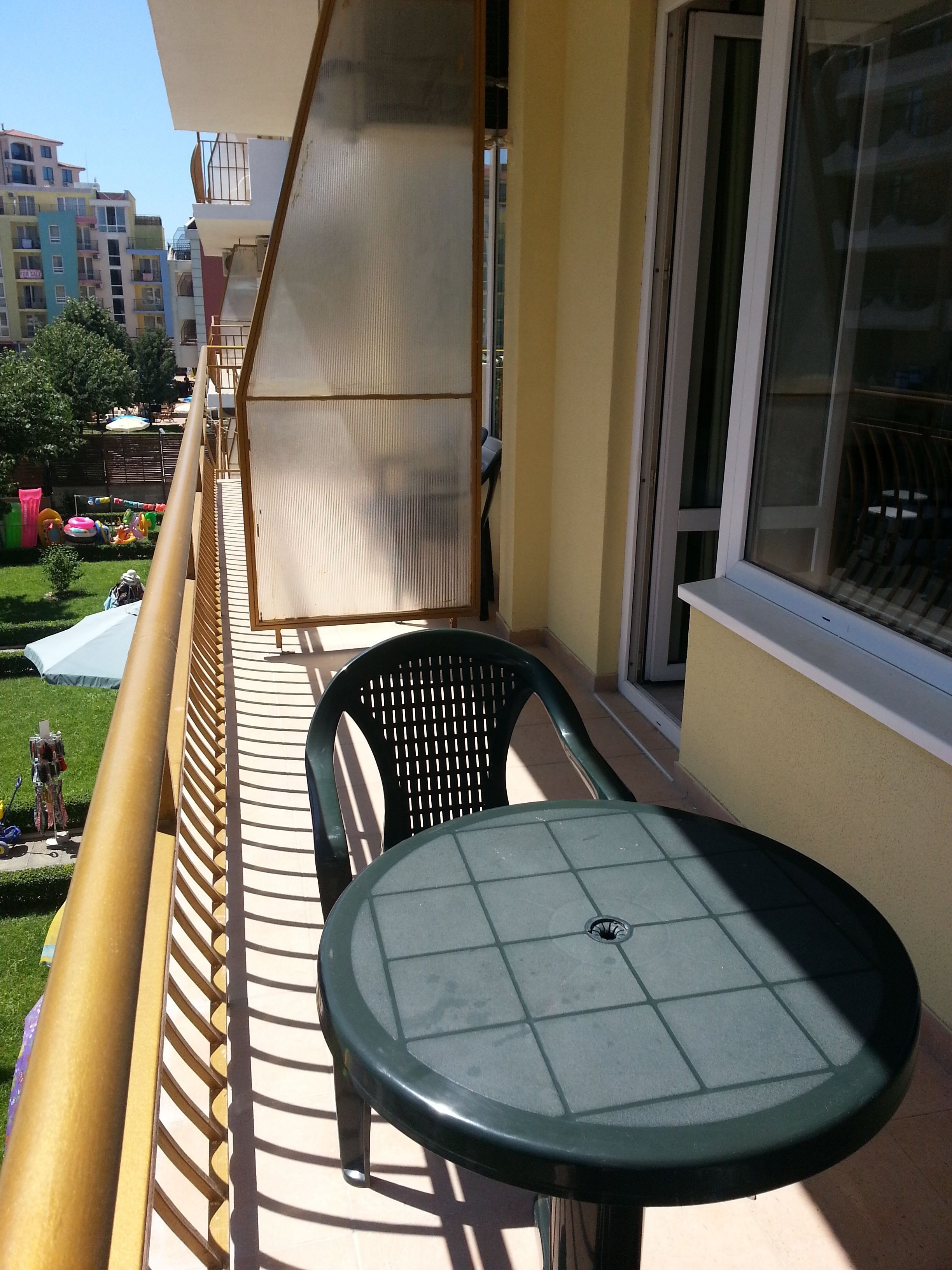 Un balcón con mesa y sillas, con vistas a un jardín y edificios.