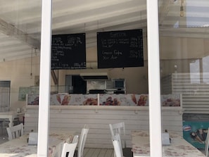 A restaurant with a counter and chairs, a chalkboard menu, and a television. - Menada Rocamar Apartments (Tsarevo)