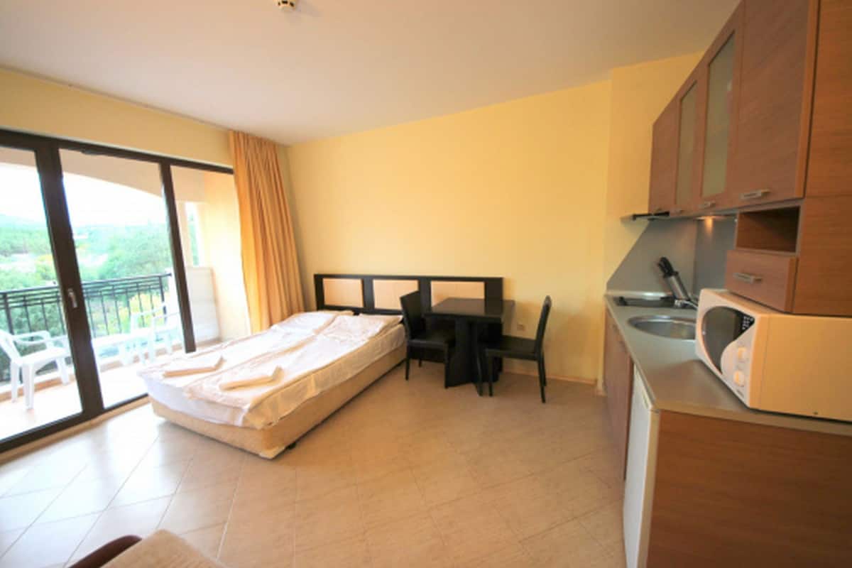 Een compacte kamer met een bed, een klein tafeltje en een kitchenette.