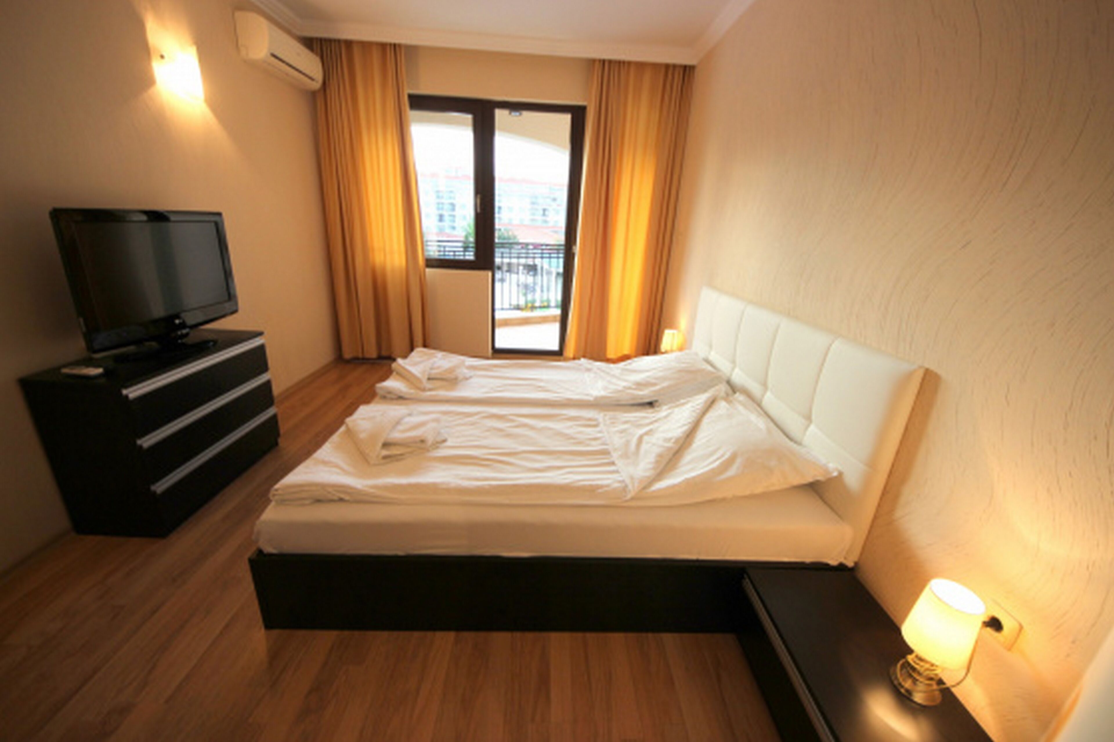 A hotel room with a bed, a TV on a dresser, and a window with curtains.