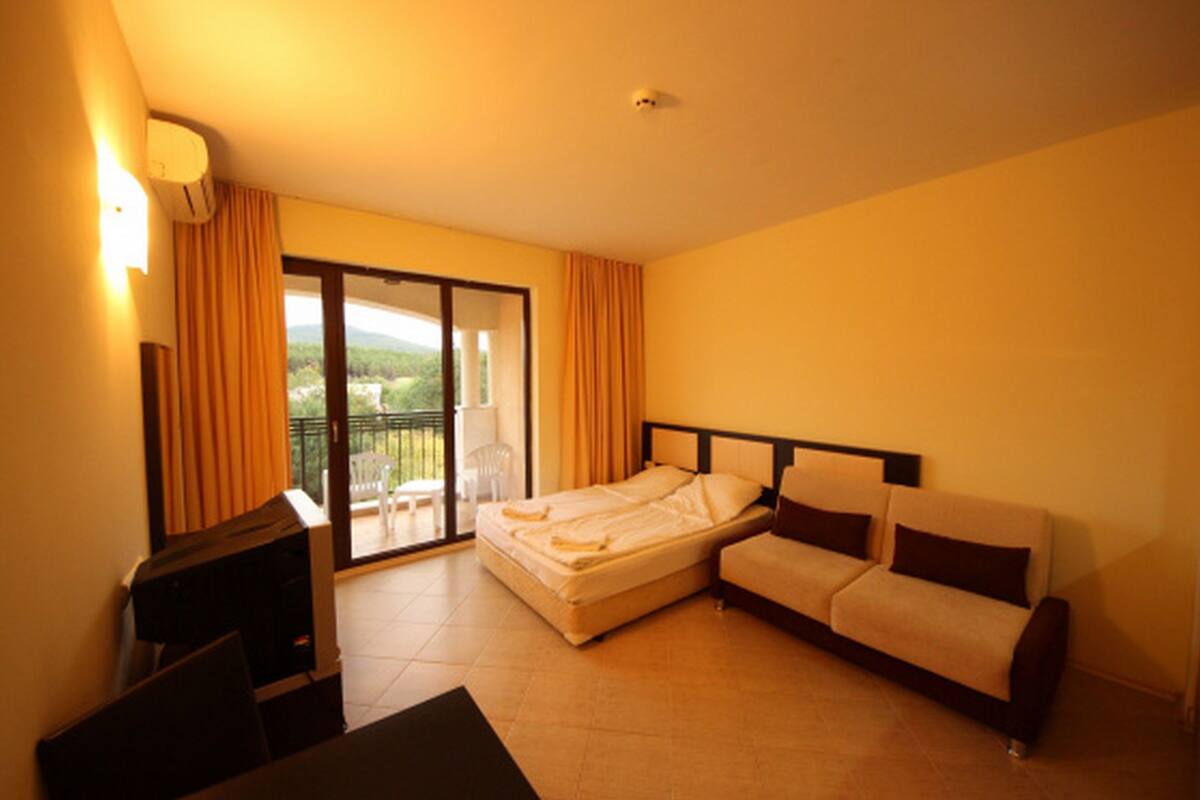 Een hotelkamer met een bed, een bank, een televisie en een schuifdeur naar een balkon.
