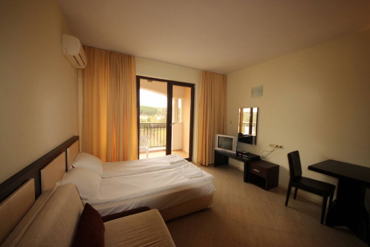 Een hotelkamer met een bed, een bureau met stoel, een televisie en een raam met gordijnen.