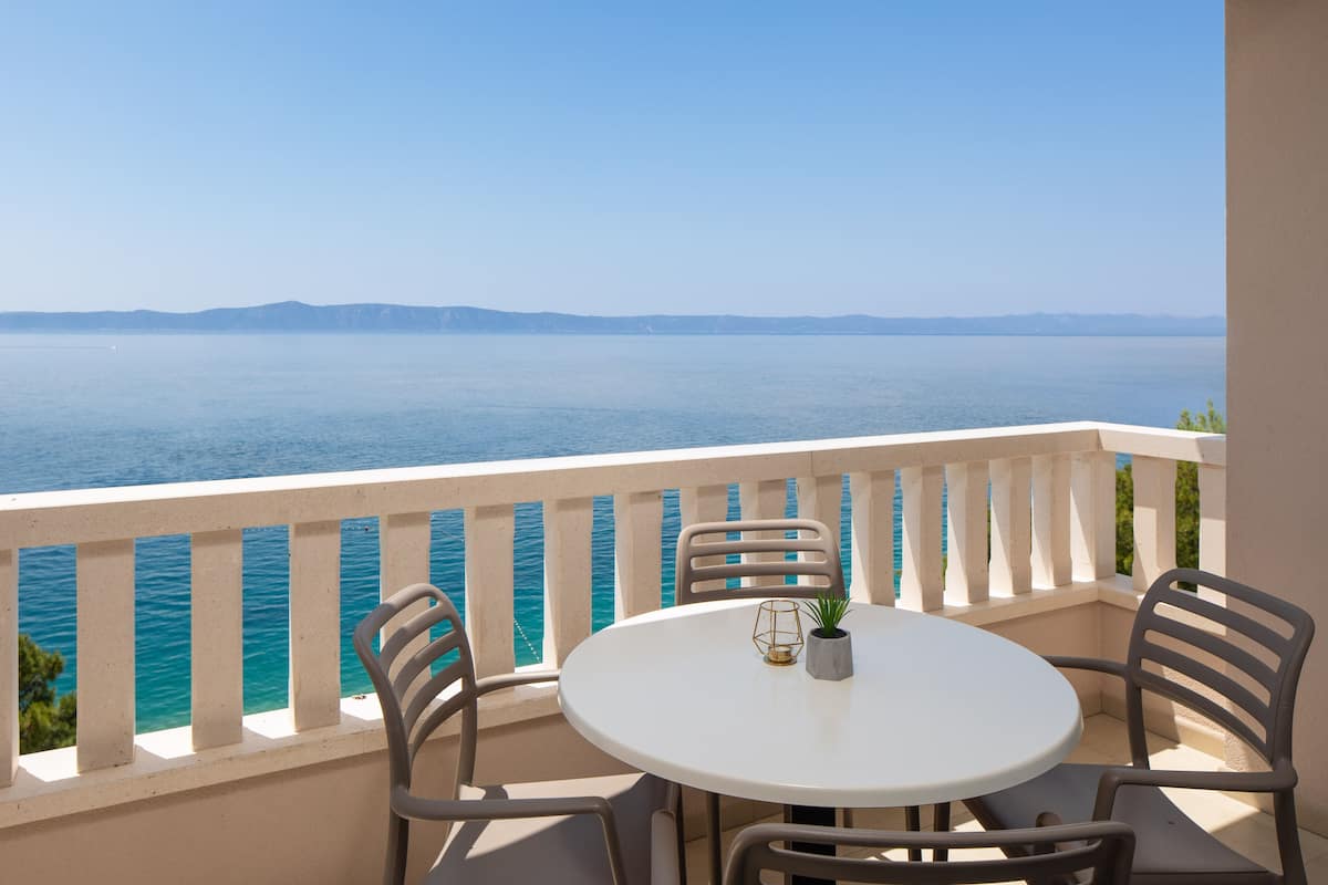 A balcony with a round table and chairs, overlooking a body of water and distant land.