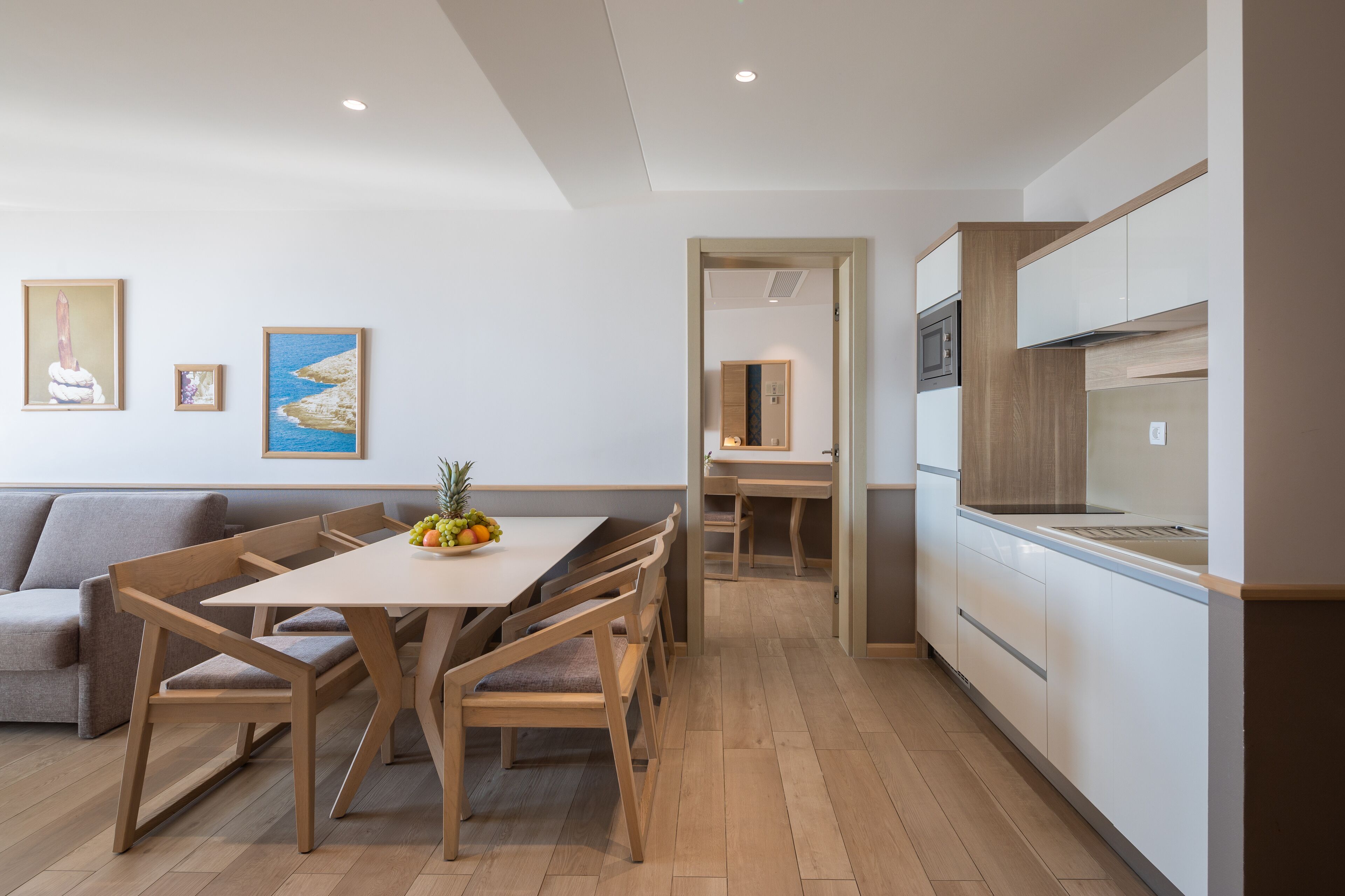 Una cocina moderna con armarios de madera, un comedor con una mesa y sillas, y un sofá gris.