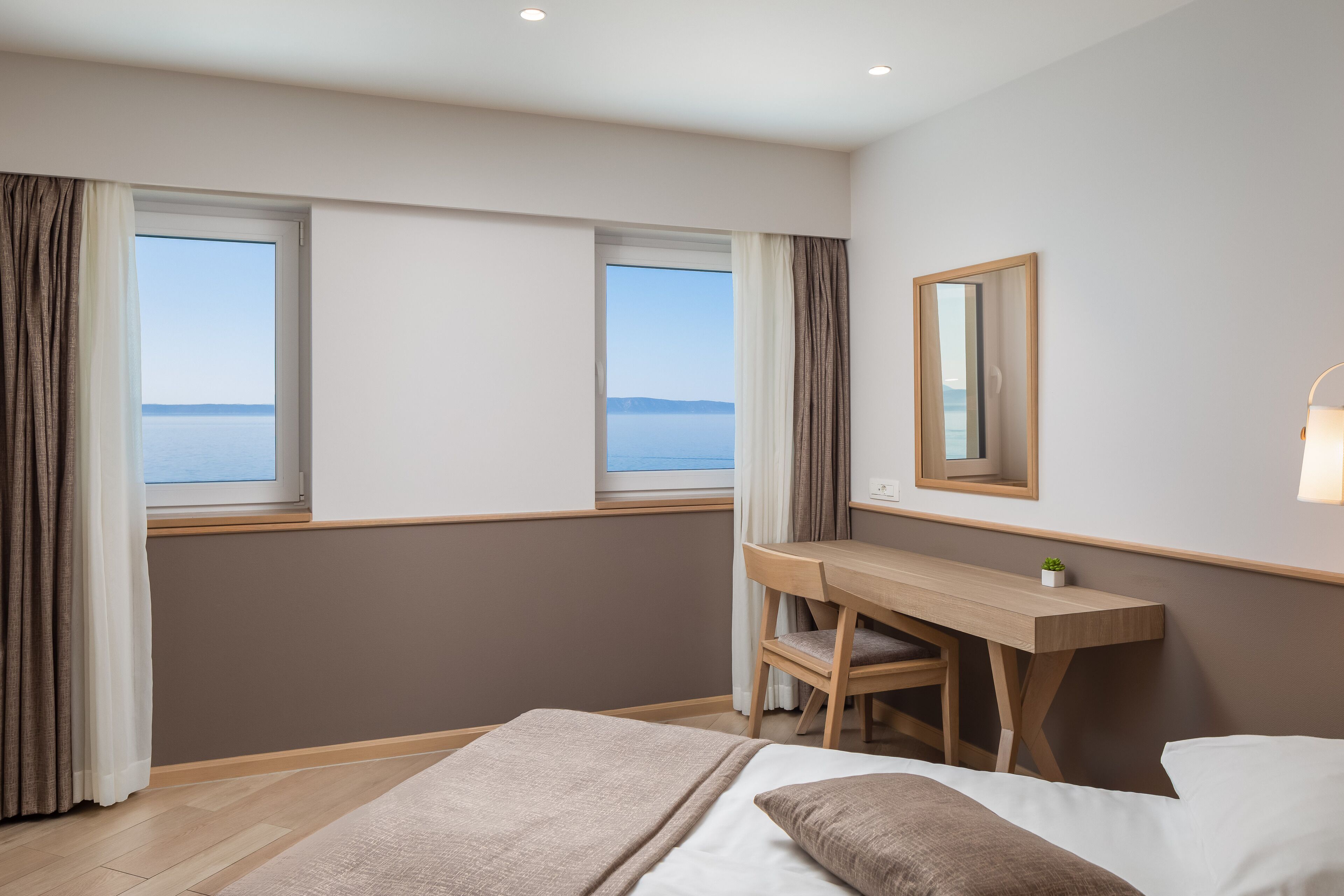 Une chambre d’hôtel avec un lit, un bureau et une vue sur la mer grâce à de grandes fenêtres.