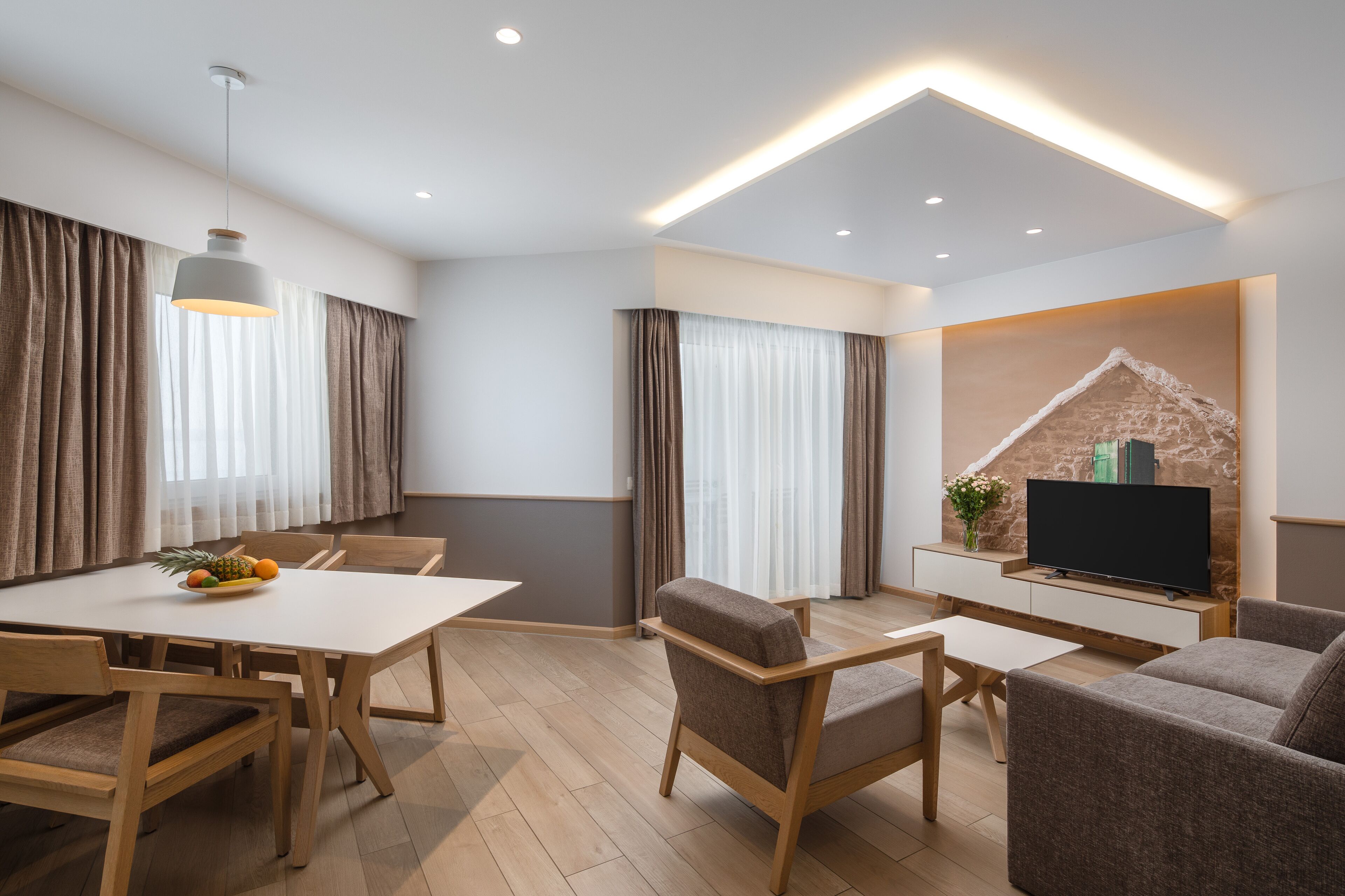 A modern living room with a dining area, wooden furniture, a flat-screen TV, and a stone accent wall.