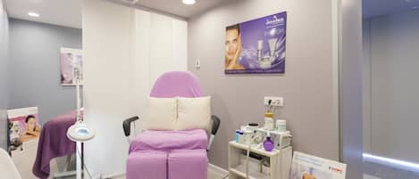 A modern spa room with a massage chair, a foot bath, and a shelf with skincare products.