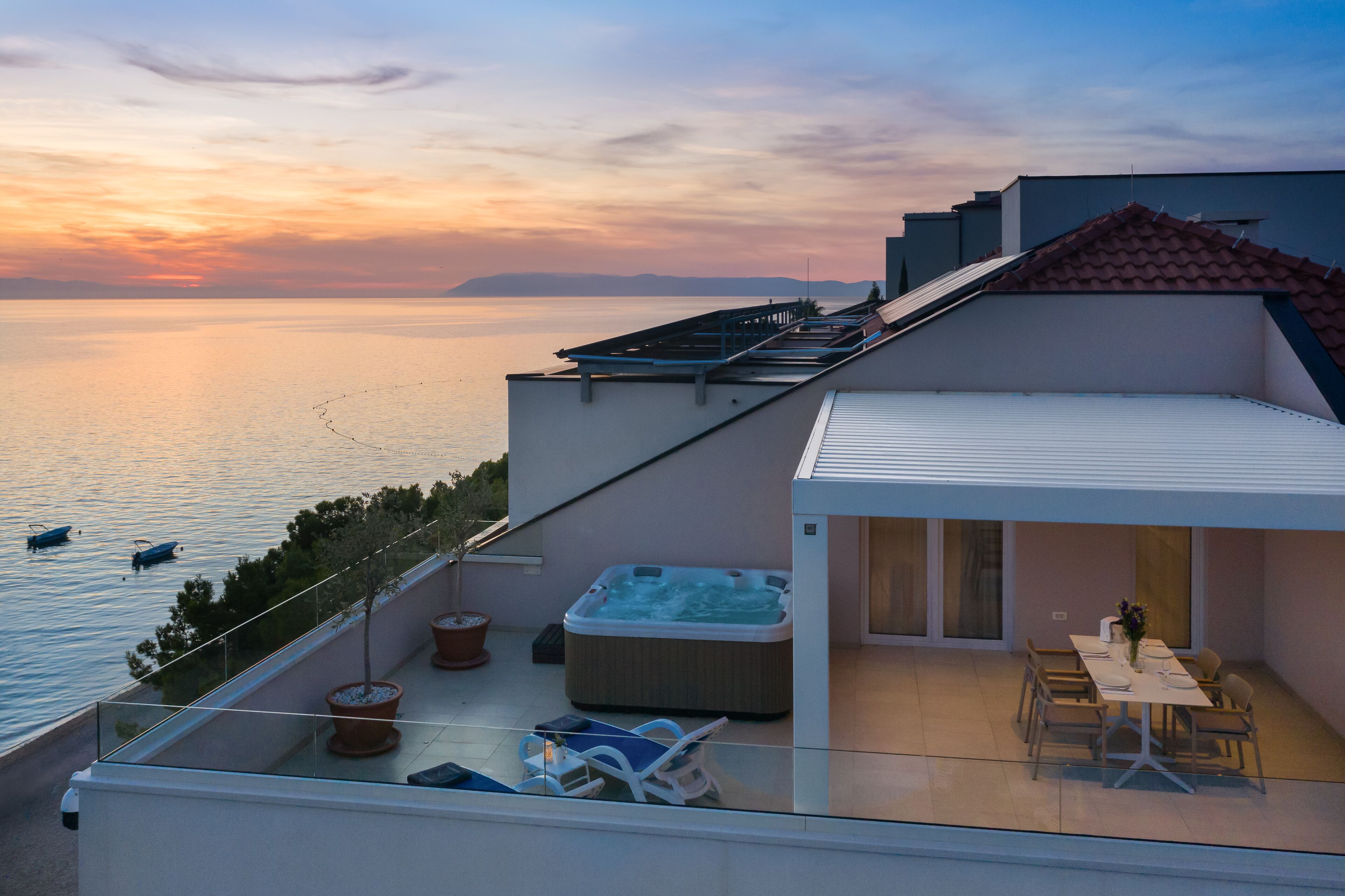 Une terrasse sur le toit avec un jacuzzi, un espace repas et une vue sur la mer au coucher du soleil.