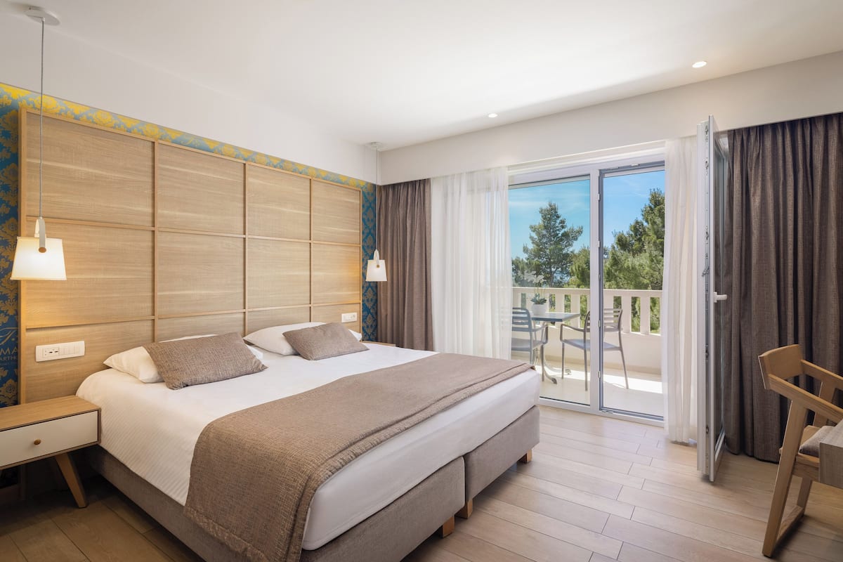 A hotel room with a large bed, a nightstand, a chair, and a balcony with a view.