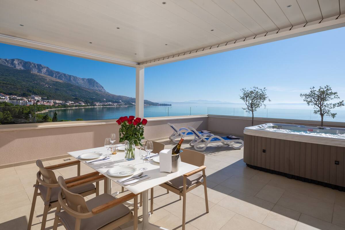 A terrace with a table set for dining, a hot tub, and a scenic view of a lake and mountains.