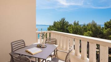 A balcony with a table and chairs, overlooking a coastal landscape with trees and the sea.