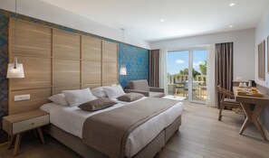 A hotel room with a large bed, a desk with a chair, a balcony with a table and chairs, and a view of the outdoors. - Hotel Tamaris (Tucepi)