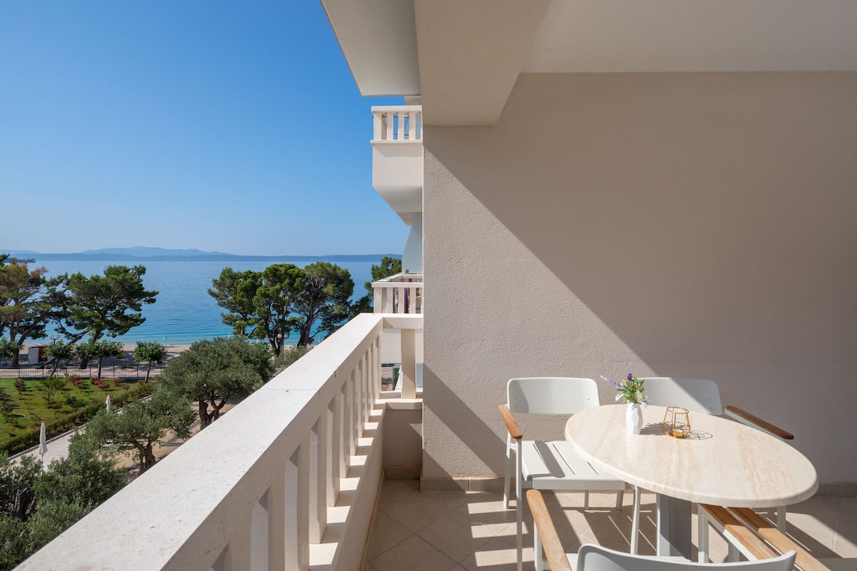 A balcony with a round table and chairs, overlooking a body of water and trees.